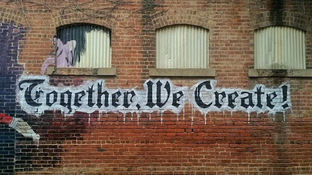 Brick wall with the words Together We Create painted on it.